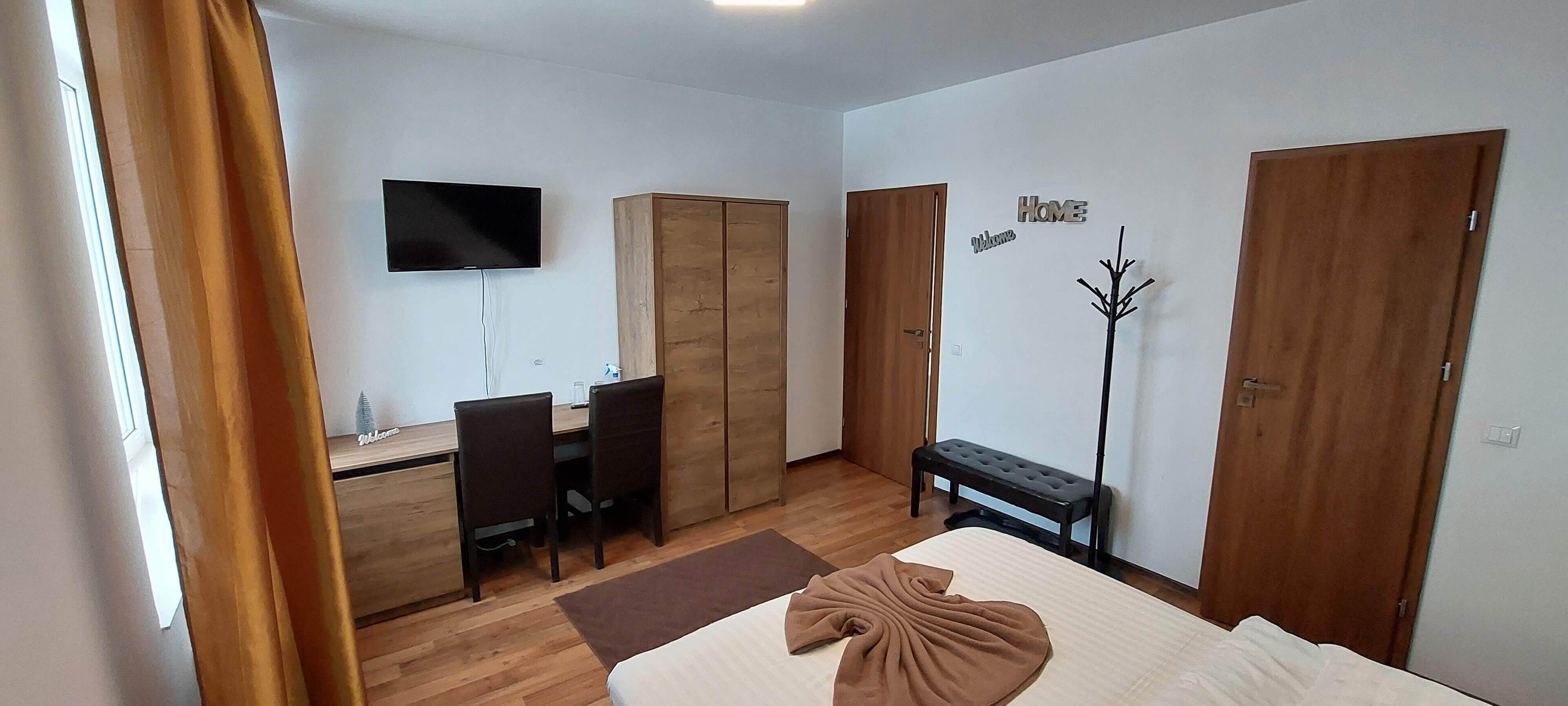 Una habitación de hotel con cama, escritorio, dos sillas, televisor y armario.
