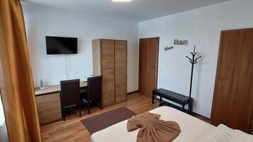 Una habitación de hotel con cama, escritorio, dos sillas, televisor y armario.