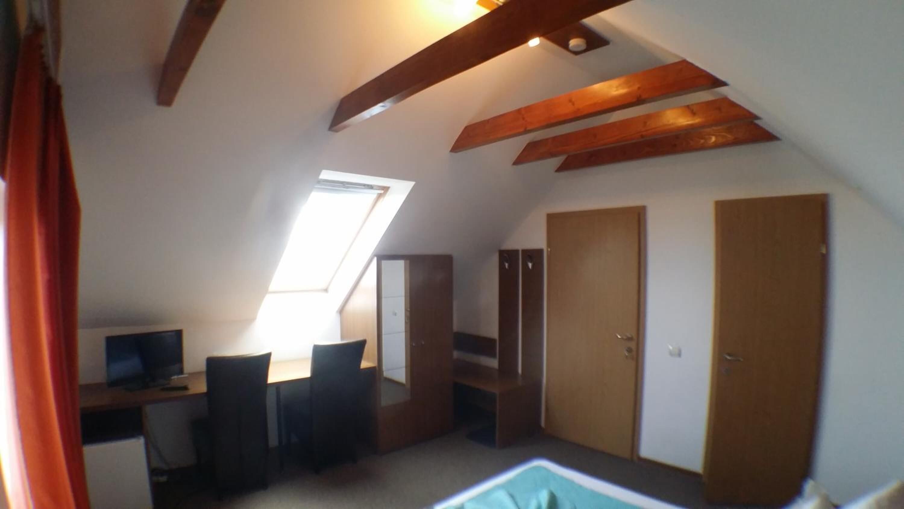 Ein Zimmer mit schrägen Wänden, einem Dachfenster, einem Schreibtisch mit Stuhl und zwei Kleiderschränken.