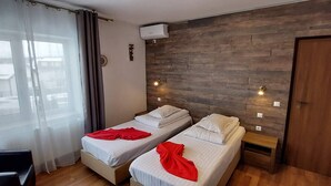 Una habitación de hotel con dos camas individuales, una pared decorativa de madera, una ventana con cortinas translúcidas y una puerta.