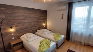 Habitación de hotel con dos camas, un cabecero de madera, vistas a la ciudad y una cortina.