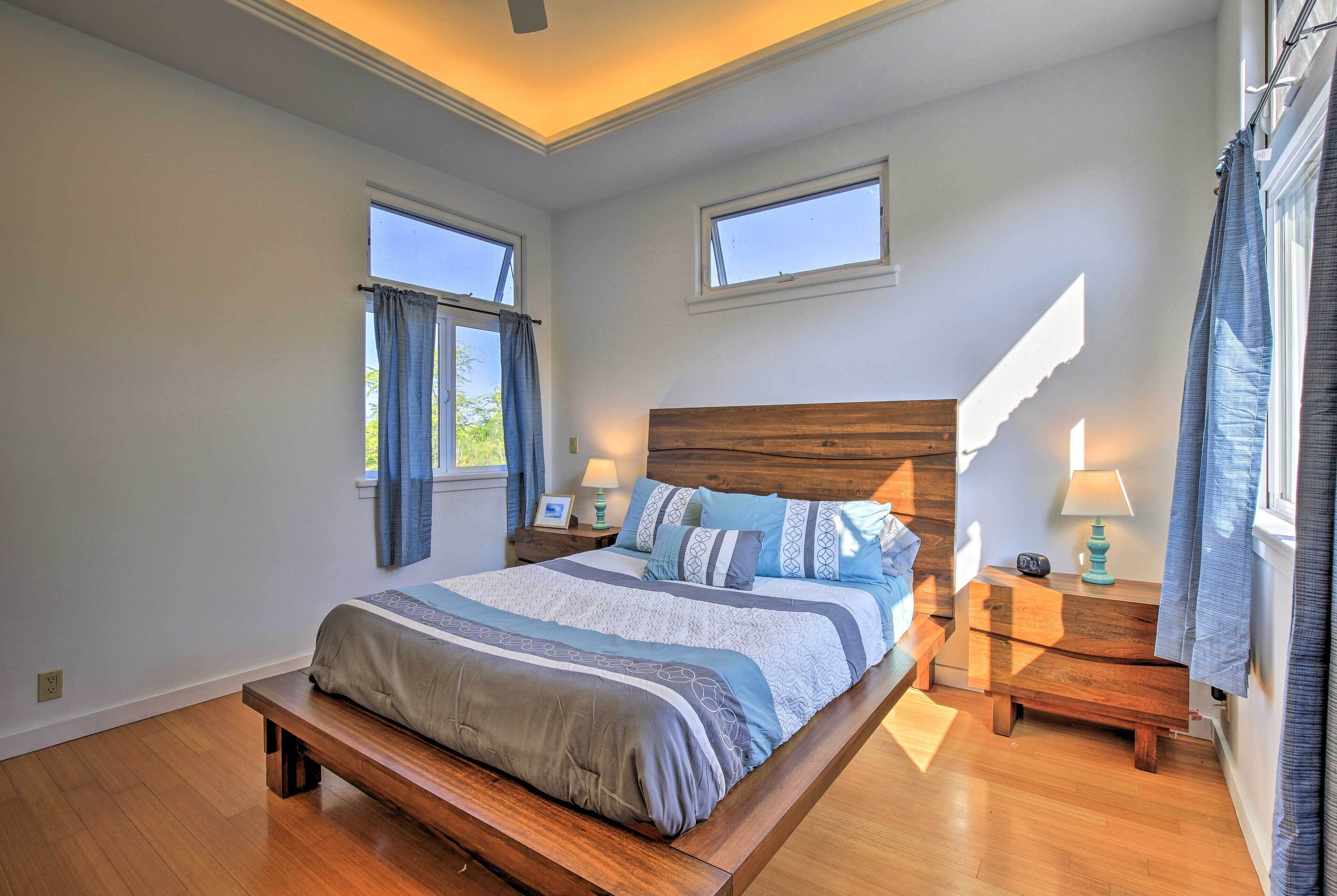 Une chambre avec un grand lit, deux tables de chevet avec des lampes, un banc au pied du lit et deux fenêtres avec des rideaux.