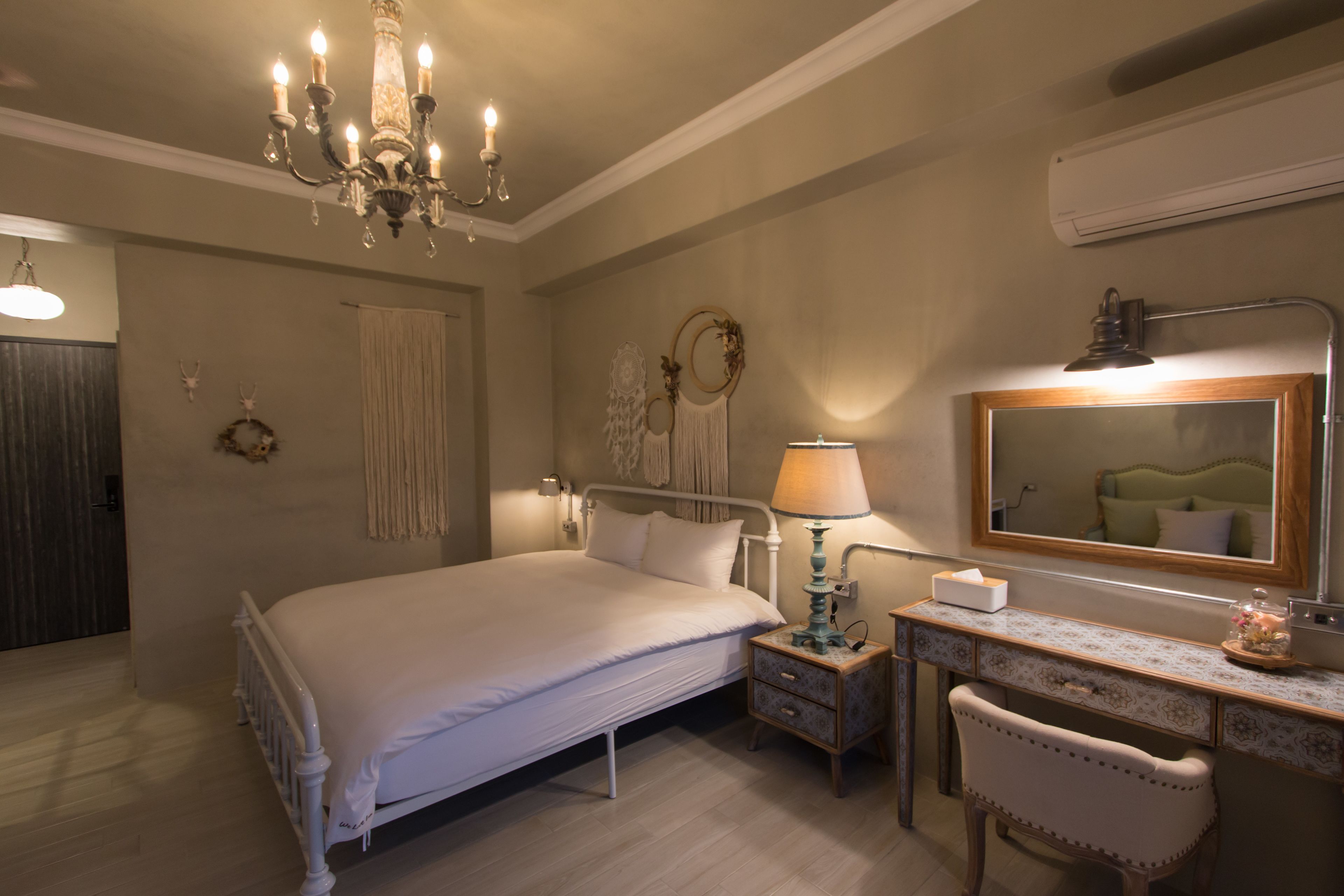 A bedroom with a bed, bedside table, lamp, dresser, mirror, and decorative wall pieces.