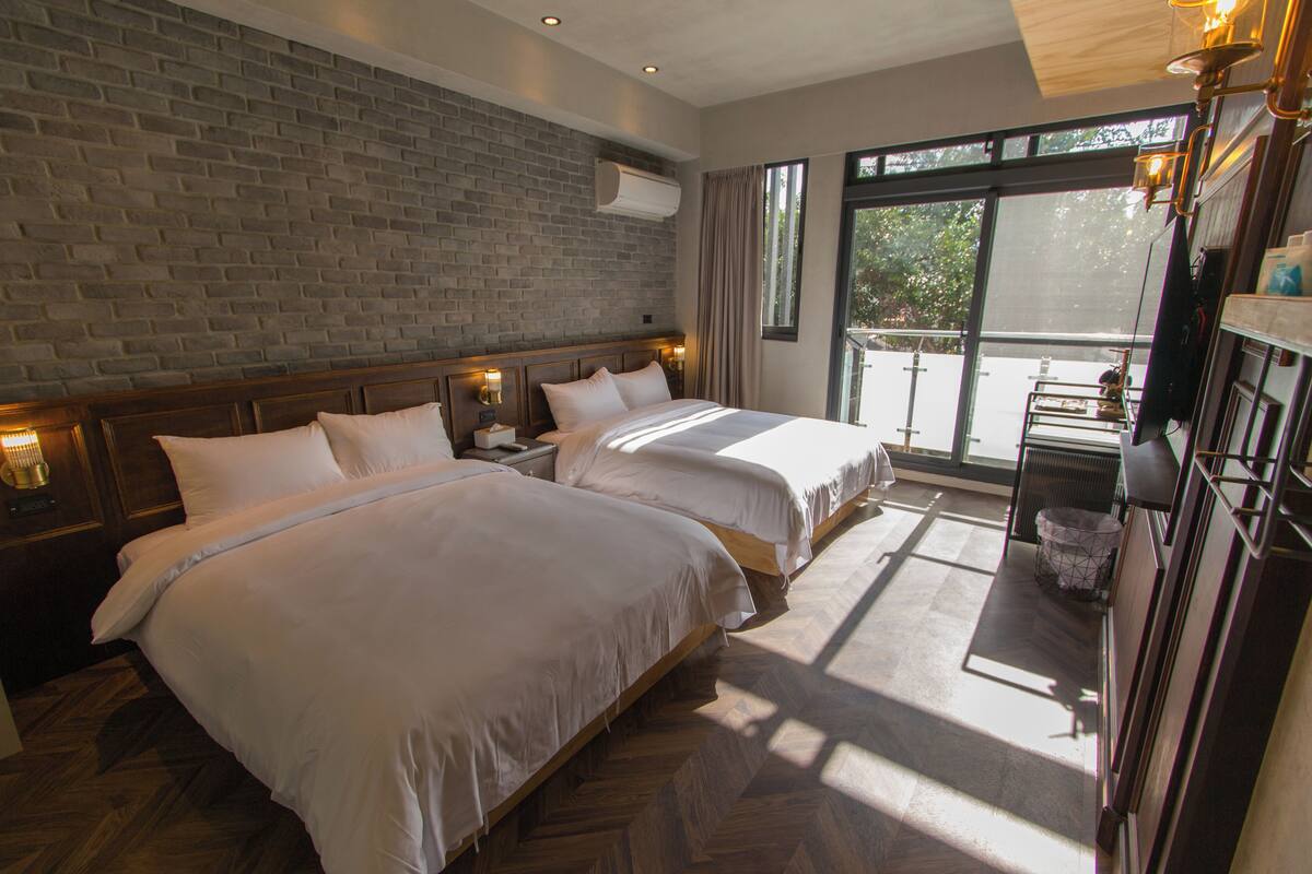 Une chambre d’hôtel avec deux lits, un mur en briques, un balcon et un plancher en bois.