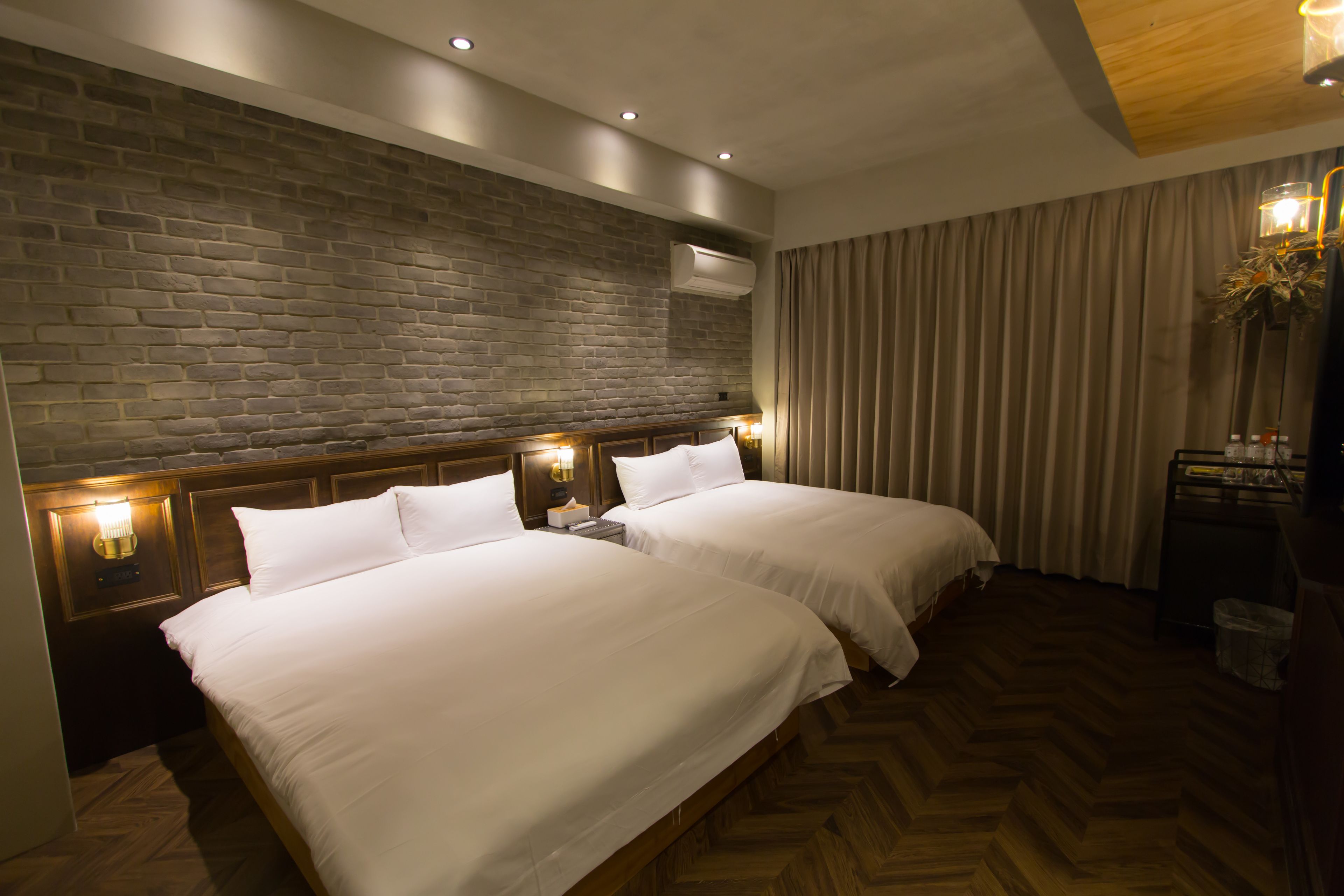Une chambre d’hôtel avec deux lits, des têtes de lit en bois, un mur en briques et un parquet disposé en chevrons.
