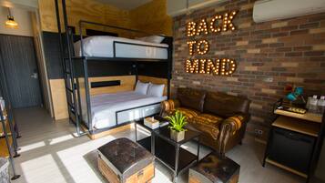 A cozy room with bunk beds, a leather sofa, a coffee table, and a wall with illuminated 'BACK TO MIND' sign.