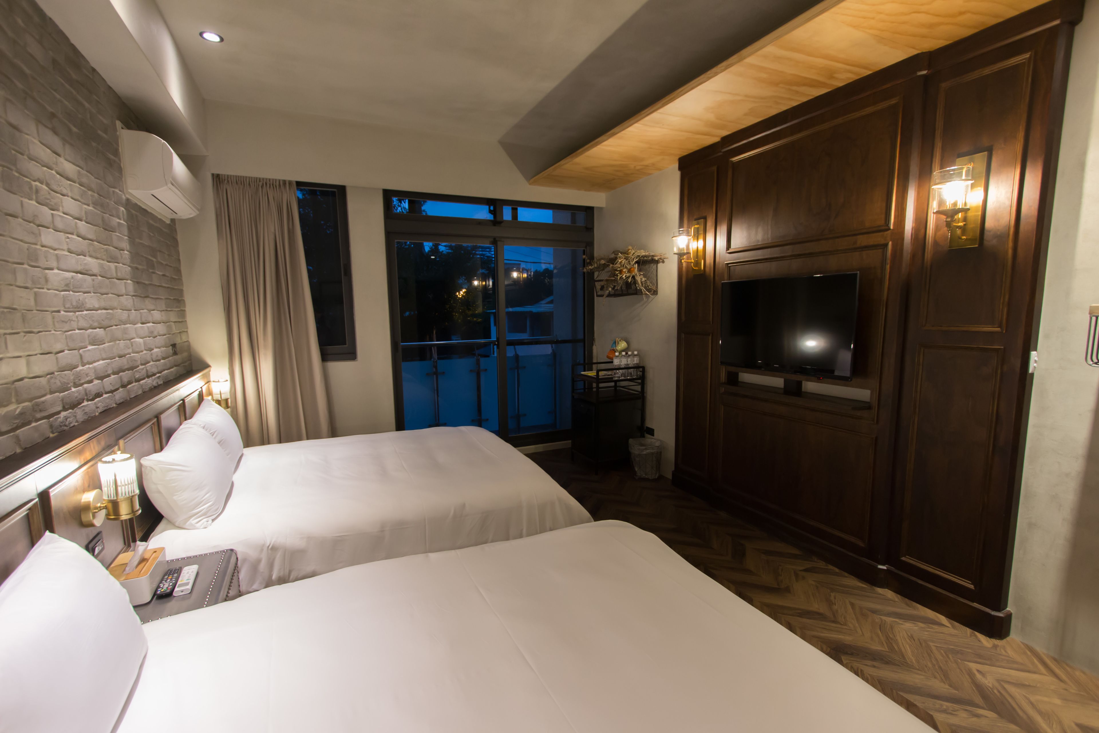 A hotel room with two beds, a TV, a wooden cabinet, and a window with curtains.