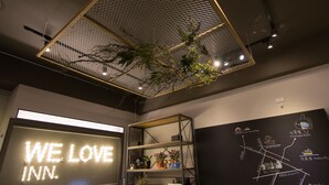 Un interior moderno con un cartel que dice 'WE LOVE INN', una estantería metálica con plantas y un mapa en la pared.