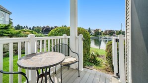 Een overdekt buitengebied met een tafel en stoelen, een witte balustrade, en uitzicht op water en groen.