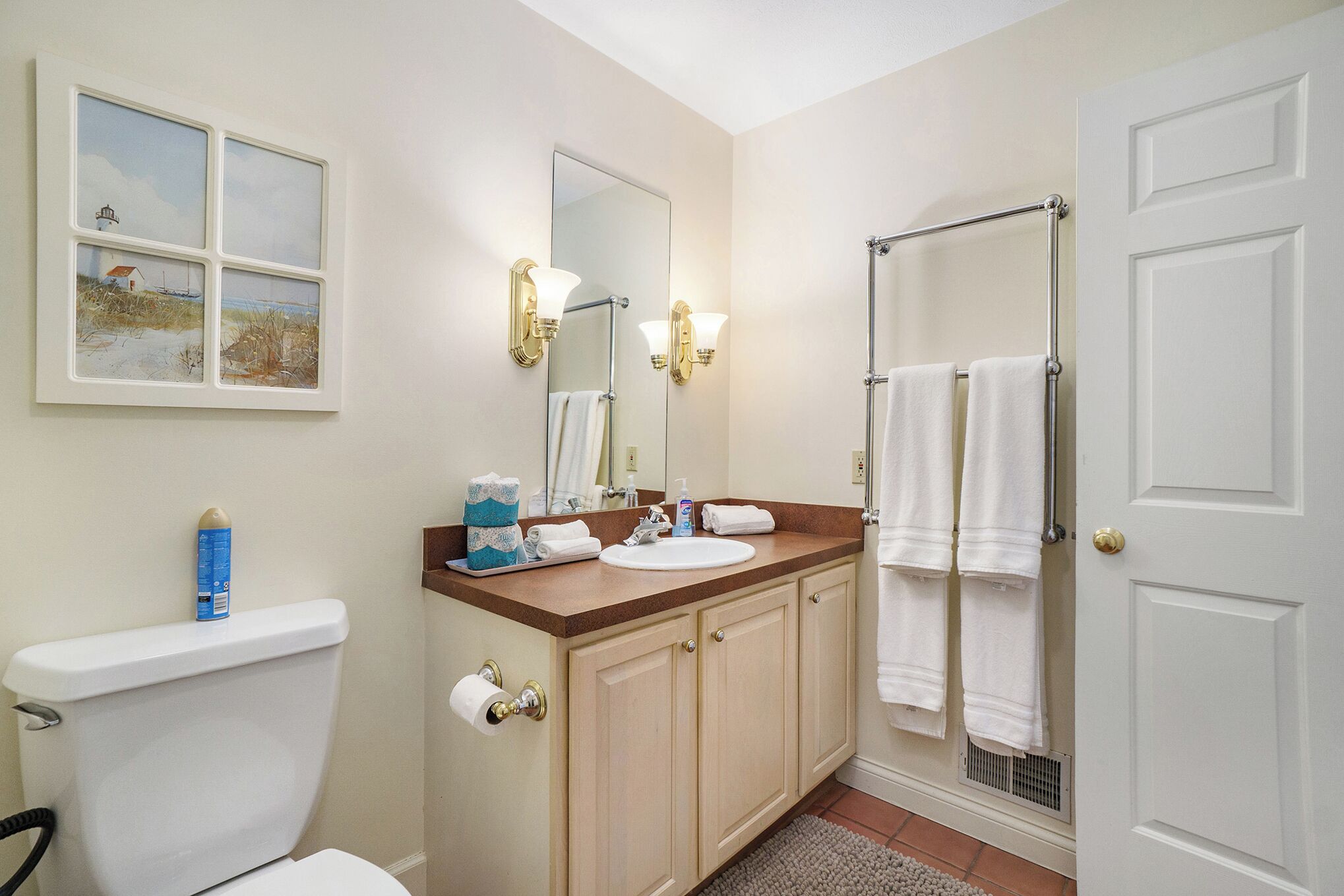 Une salle de bain équipée de toilettes, d’un lavabo et d’une douche. Des serviettes sont accrochées à la porte de la douche.