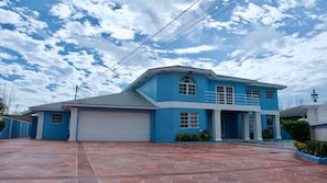 Una casa de dos pisos con fachada azul, puerta de garaje blanca y entrada con tejas rojas.