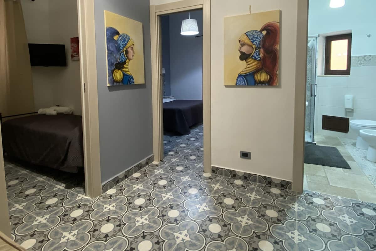 A hotel corridor with patterned flooring, artwork on the walls, and an air conditioning unit on the ceiling.