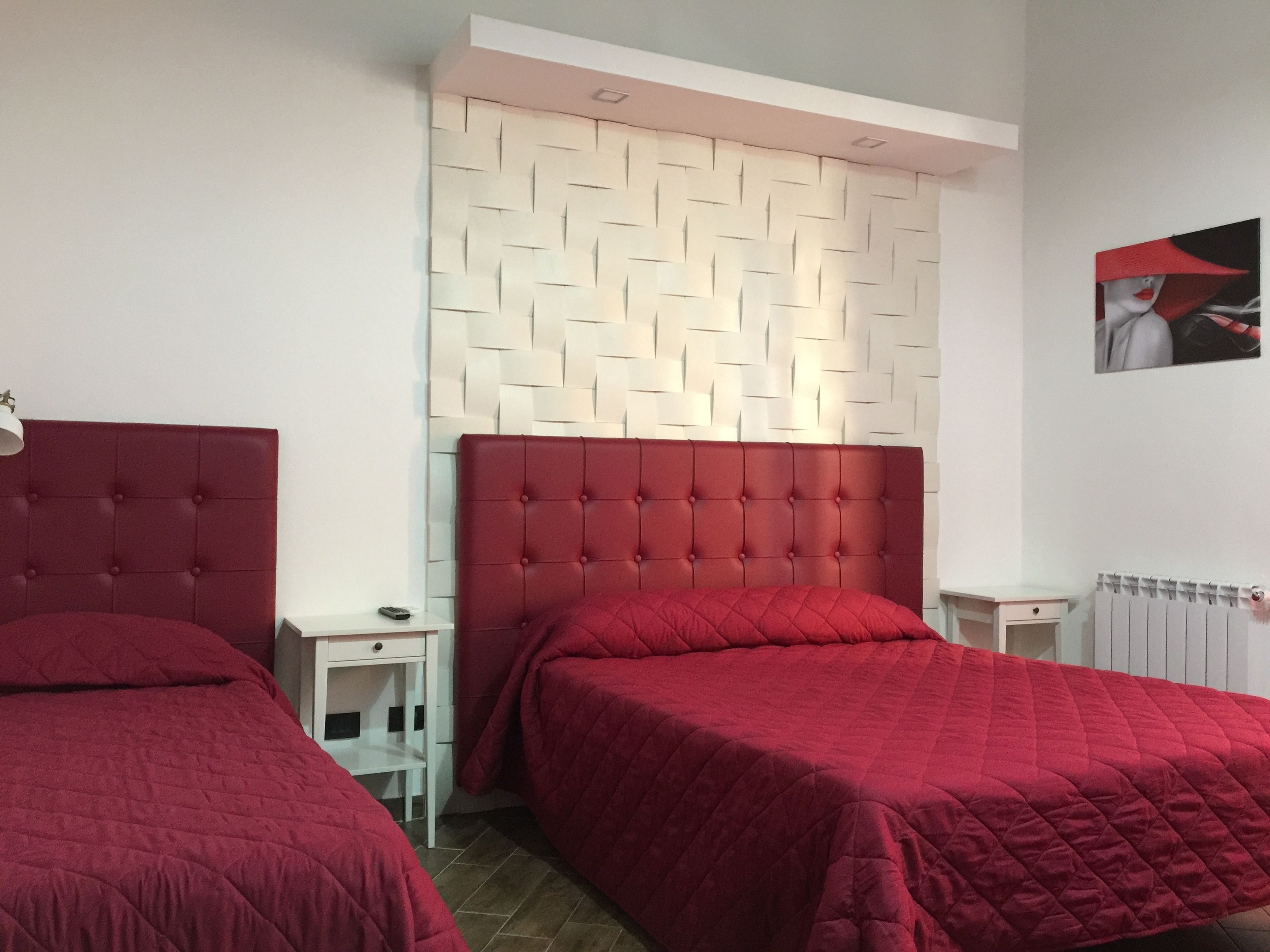 Een hotelkamer met twee bedden, elk voorzien van een rode hoofdbord, een witte nachtkastje en een witte muur met een geometrisch patroon.