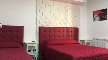 Een hotelkamer met twee bedden, elk voorzien van een rode hoofdbord, een witte nachtkastje en een witte muur met een geometrisch patroon.