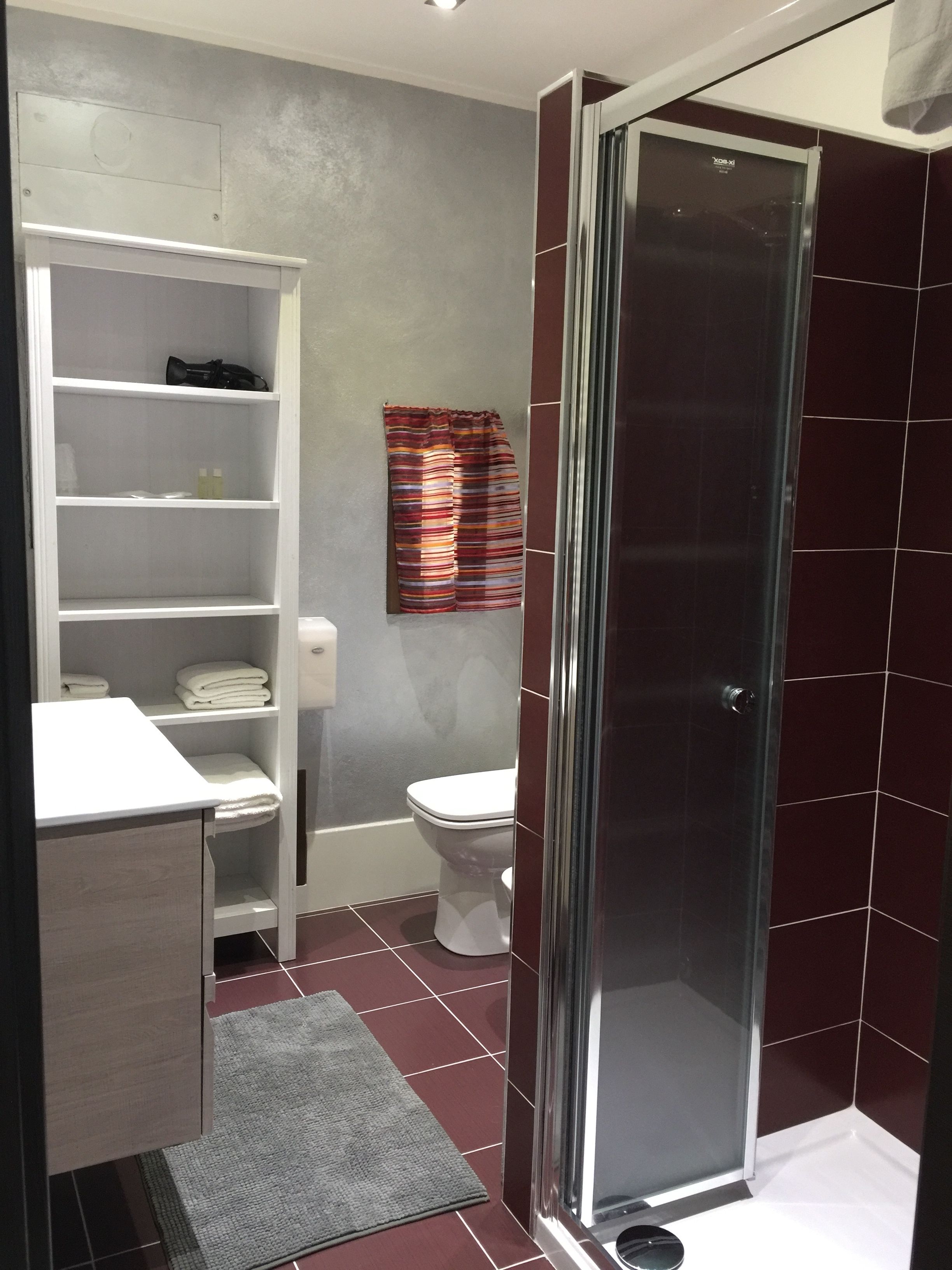 Une salle de bain moderne avec une douche à l’italienne, des toilettes et une étagère intégrée de couleur blanche.