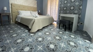A hotel room with a bed, a desk, and patterned floor tiles.