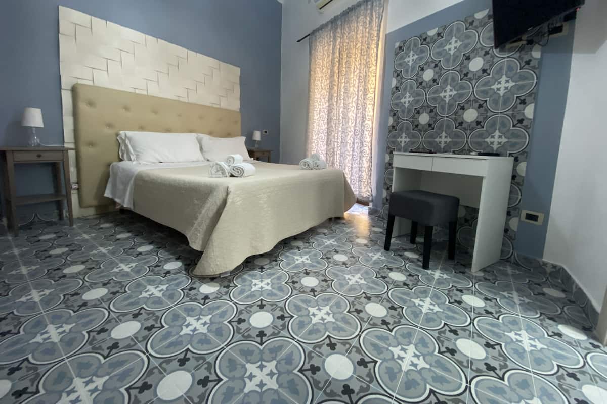 A hotel room with a bed, a desk, and patterned floor tiles.
