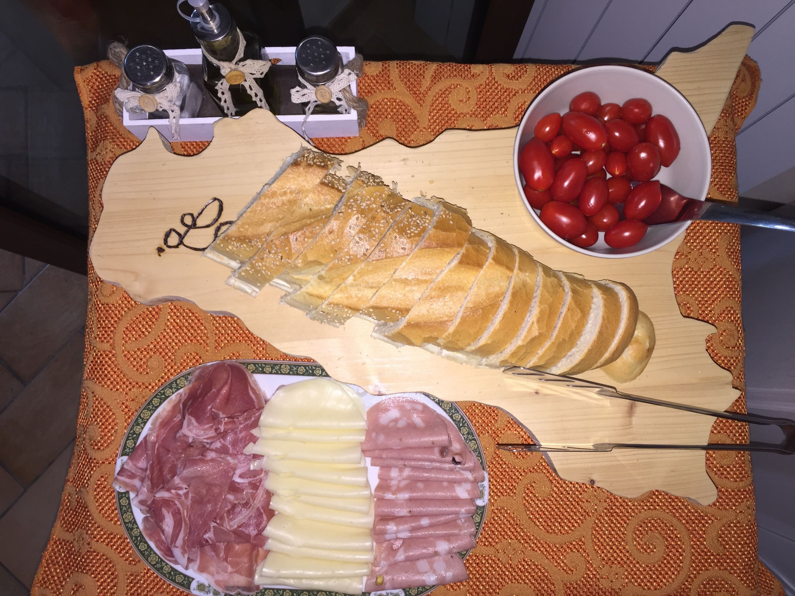 Una tabla de madera con rebanadas de pan, un cuenco de tomates cherry y un plato de embutidos.