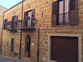 Un edificio de piedra con garaje en la planta baja, balcones en el piso superior con jardineras, y una puerta de garaje marrón.