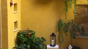 A yellow-walled room with a mounted TV, potted plants, a lantern, and a small white table.
