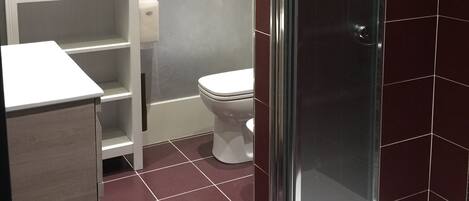 A bathroom with a glass-enclosed shower, a white toilet, a white shelf unit, and a mirror on the wall.