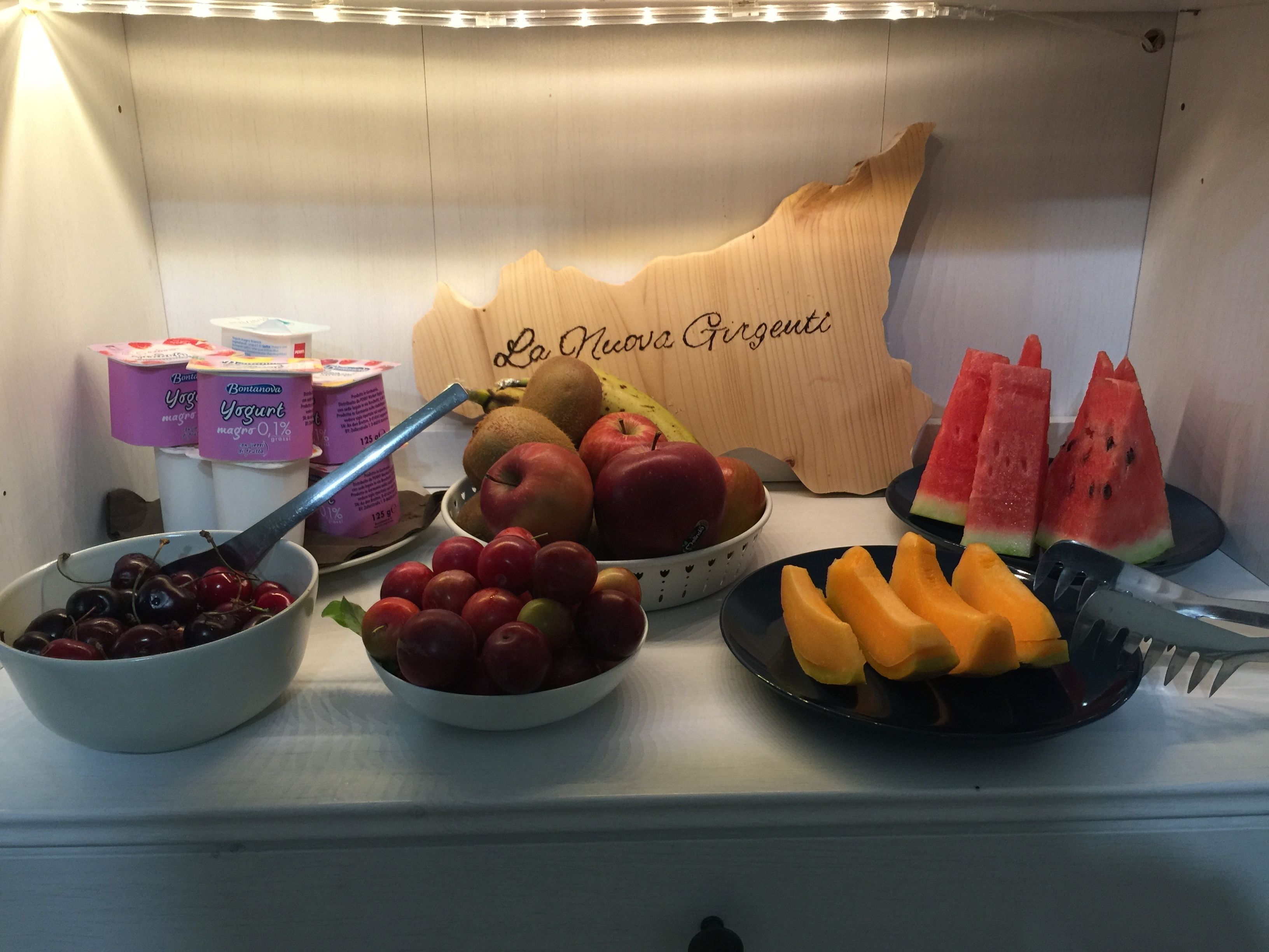 A breakfast buffet with various fruits, yogurt, and a wooden sign.