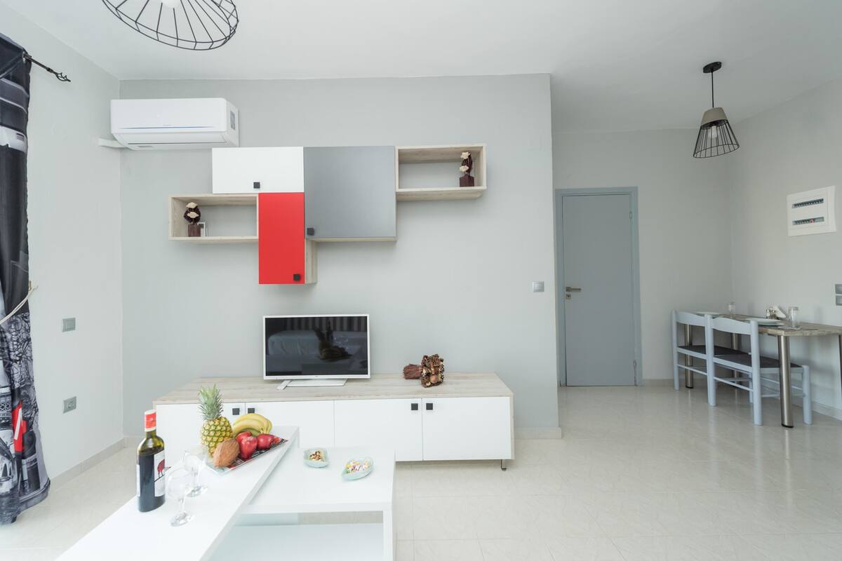Un salon moderne avec un meuble de rangement blanc pour l’équipement audiovisuel, un téléviseur à écran plat et un coin repas comprenant une table et des chaises.