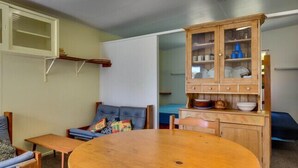 Un espacio habitable compacto con una mesa redonda de madera, un sofá, un mueble con puertas de vidrio y una cama al fondo.