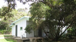 Un edificio pequeño de una sola planta con tejado verde, un sendero de piedra que lleva a la entrada y un césped verde y exuberante.