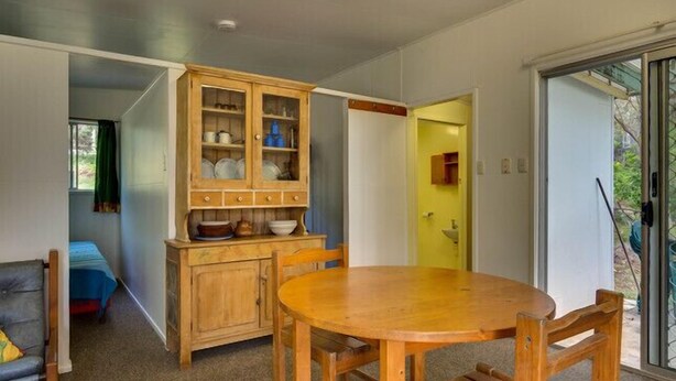 Un comedor con una mesa y sillas de madera, un mueble con vajilla, y vistas a través de un ventanal.