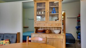 Un área de comedor con un mueble de madera que contiene vajilla y un hervidor, una mesa redonda y un sofá azul.