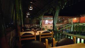 An indoor restaurant with wooden tables and chairs, a view of a bridge, and a sign for 'KIYITI'. - Hotel Vassi Palaze (Chengalpattu)
