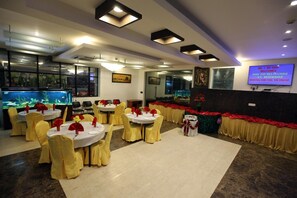 A restaurant with round tables, yellow chairs, and a large fish tank. - Hotel Vassi Palaze (Chengalpattu)