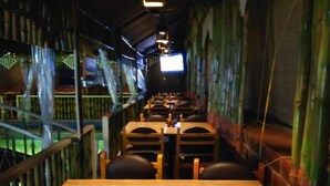 A restaurant with bamboo walls, wooden tables, and chairs. - Hotel Vassi Palaze (Chengalpattu)