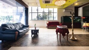 A modern living room with a black leather sofa, a red sofa, a coffee table, and a decorative table with a brass stand. - Hotel Vassi Palaze (Chengalpattu)