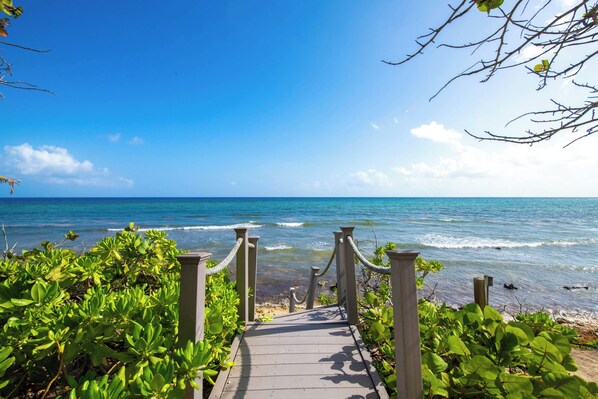 A wooden pathway leading to the beach with clear blue water and a bright sky.