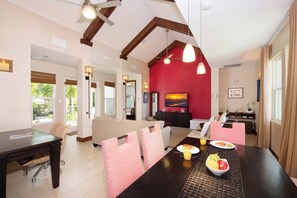 A spacious living area with a high ceiling, a dining table set with food, and a red accent wall. - Sea Orchard Retreat: Micro-Resort Near 7Mile Beach w/Private Pool & Hot Tub (West Bay)