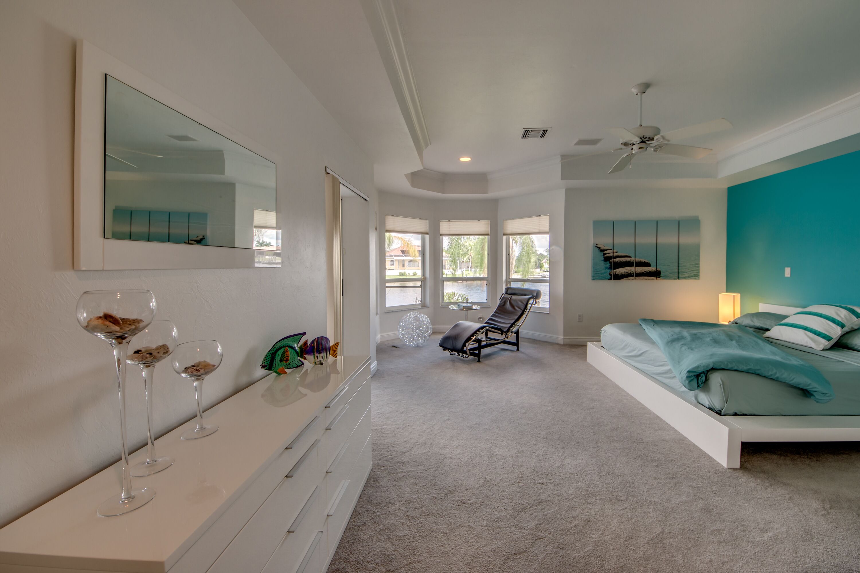 A bedroom with a bed, a chair, a vanity with a mirror, and a window with a view of the outside.