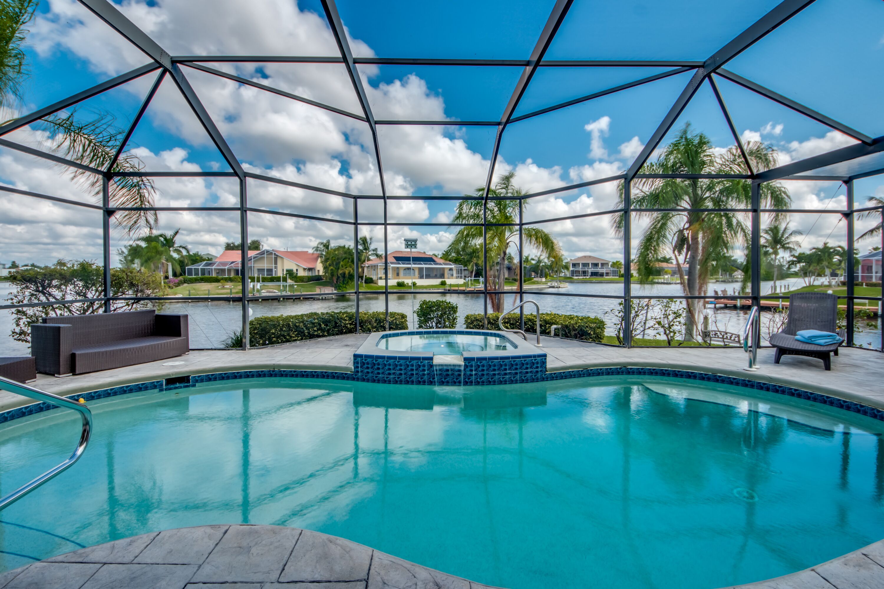 A pool area with a glass enclosure, a hot tub, and lounge chairs.