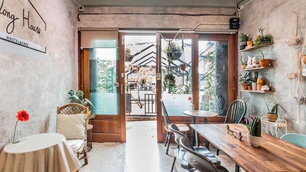 A cozy hostel with a rustic interior, featuring a wooden dining table, wicker chairs, and a variety of potted plants. - Klong House Hostel (Bangkok)