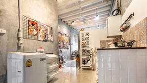 A laundry area with a large washing machine, a drying rack, and a tiled wall with a decorative pattern. - Klong House Hostel (Bangkok)