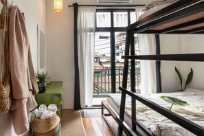 A bunk bed room with a view of a balcony and buildings. There is a green dresser with a plant and rolled towels. - Klong House Hostel (Bangkok)