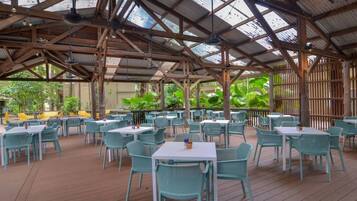 An outdoor dining area with tables and chairs, a wooden deck, and a metal roof structure.