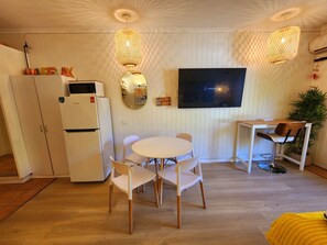 A compact living space with a dining area, a TV mounted on the wall, and a kitchenette. - Ramada Resort & Spa, Deluxe Studio Apartment.! (Port Douglas)
