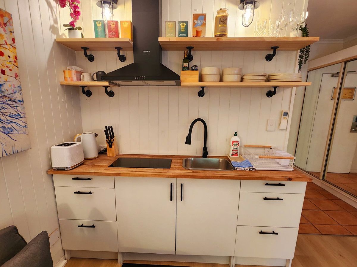 A modern kitchen with white cabinets, a wooden countertop, and black fixtures. There are shelves above the counter holding various items, and a black range hood above the stove.