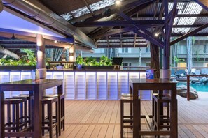 An outdoor bar area with wooden furniture and a pool in the background.