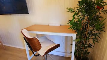 A modern room with a wooden dining table, a white chair with a wooden backrest, a large potted plant, and a flat-screen TV mounted on the wall.