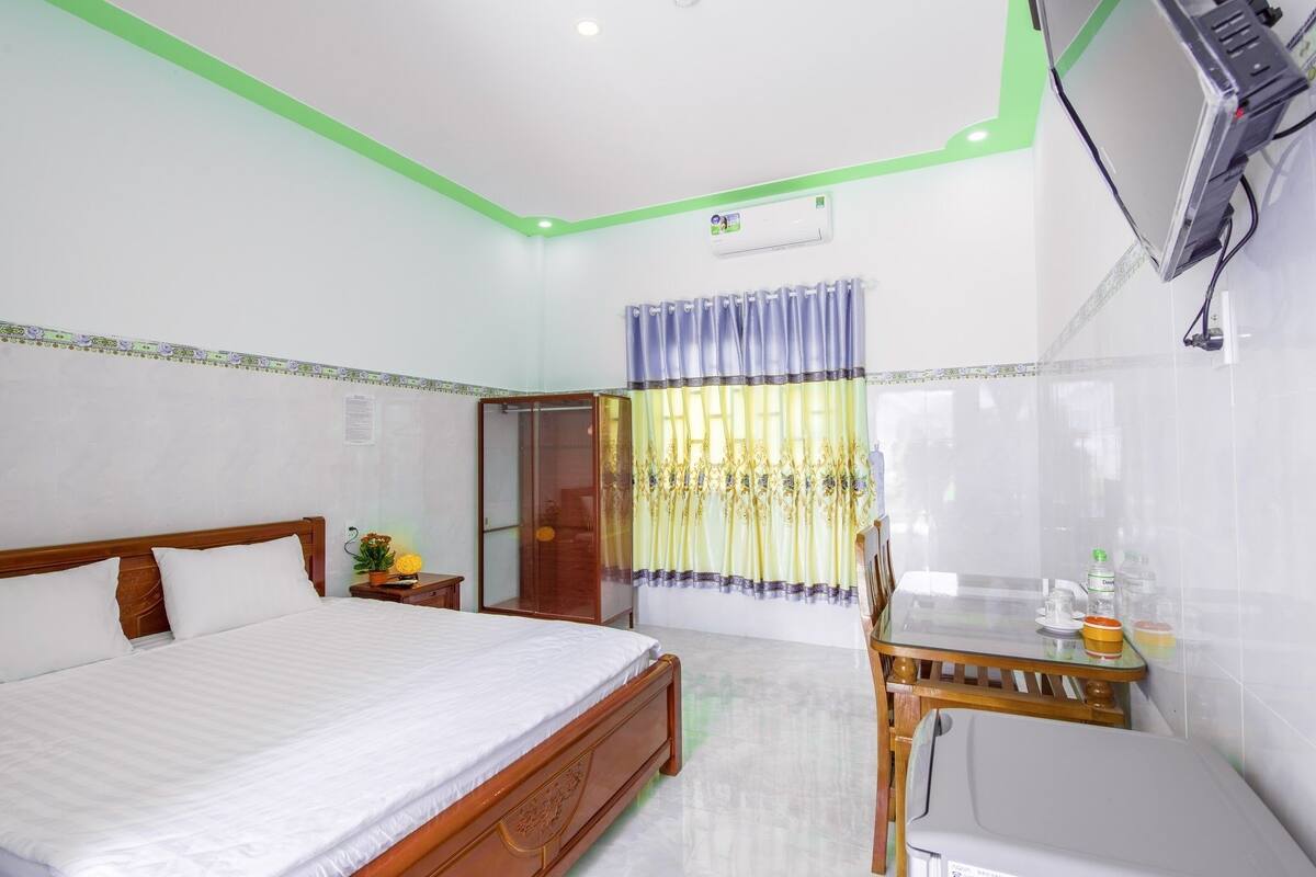 A hotel room with a bed, a desk, a chair, an air conditioner, and a window with curtains.
