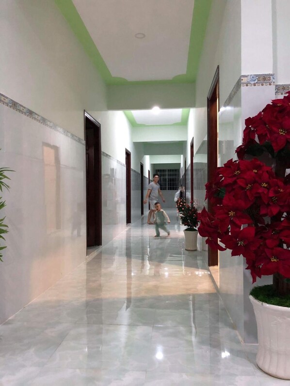 A hallway with a glossy marble floor, green ceiling, and a large potted plant with red flowers.