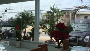 A covered outdoor seating area with a glass table and wooden chairs, surrounded by potted plants and flowers.